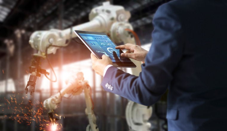 Ein Mann im Anzug steuert einen Roboterarm in einer Fabrik über ein Tablet